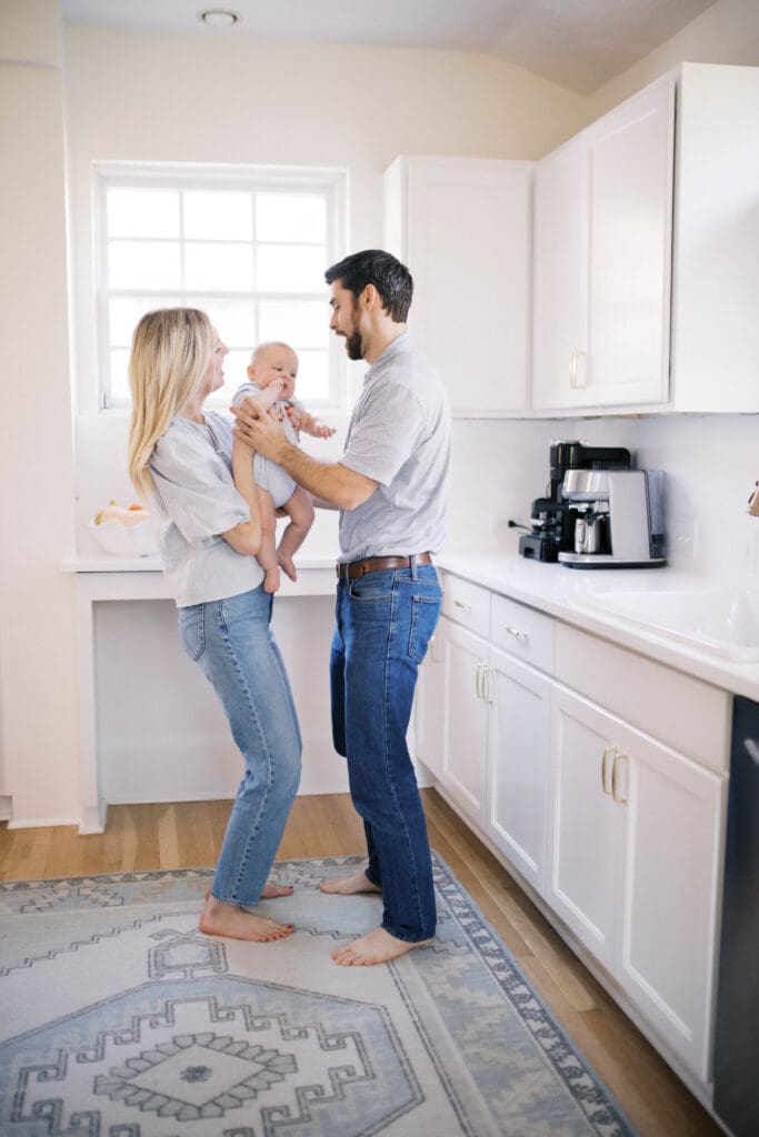 Lifestyle Newborn Photo of a mom in blue jeans and dad dancing with baby boy in the kitchen