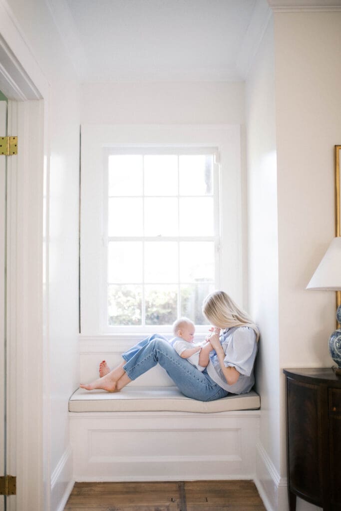 Lifestyle Newborn Photo of a mom in blue jeans kissing her baby boy's toes shot in a Jacksonville Home on the reading corner bench