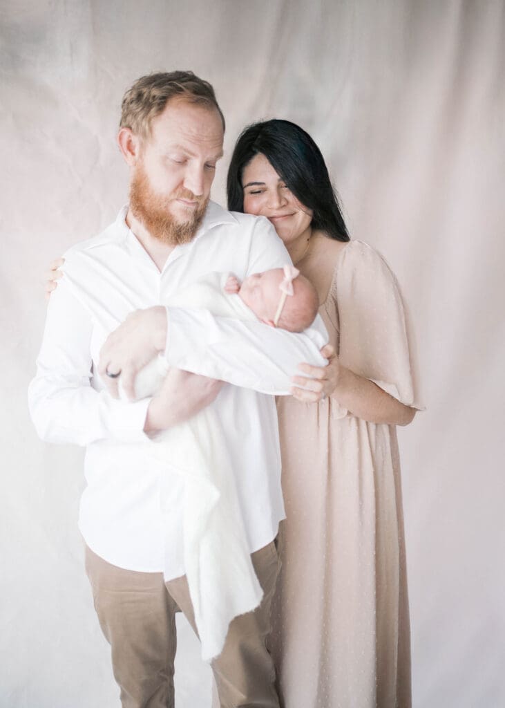 Jacksonville FL newborn photography with parents cuddling their baby in natural light studio