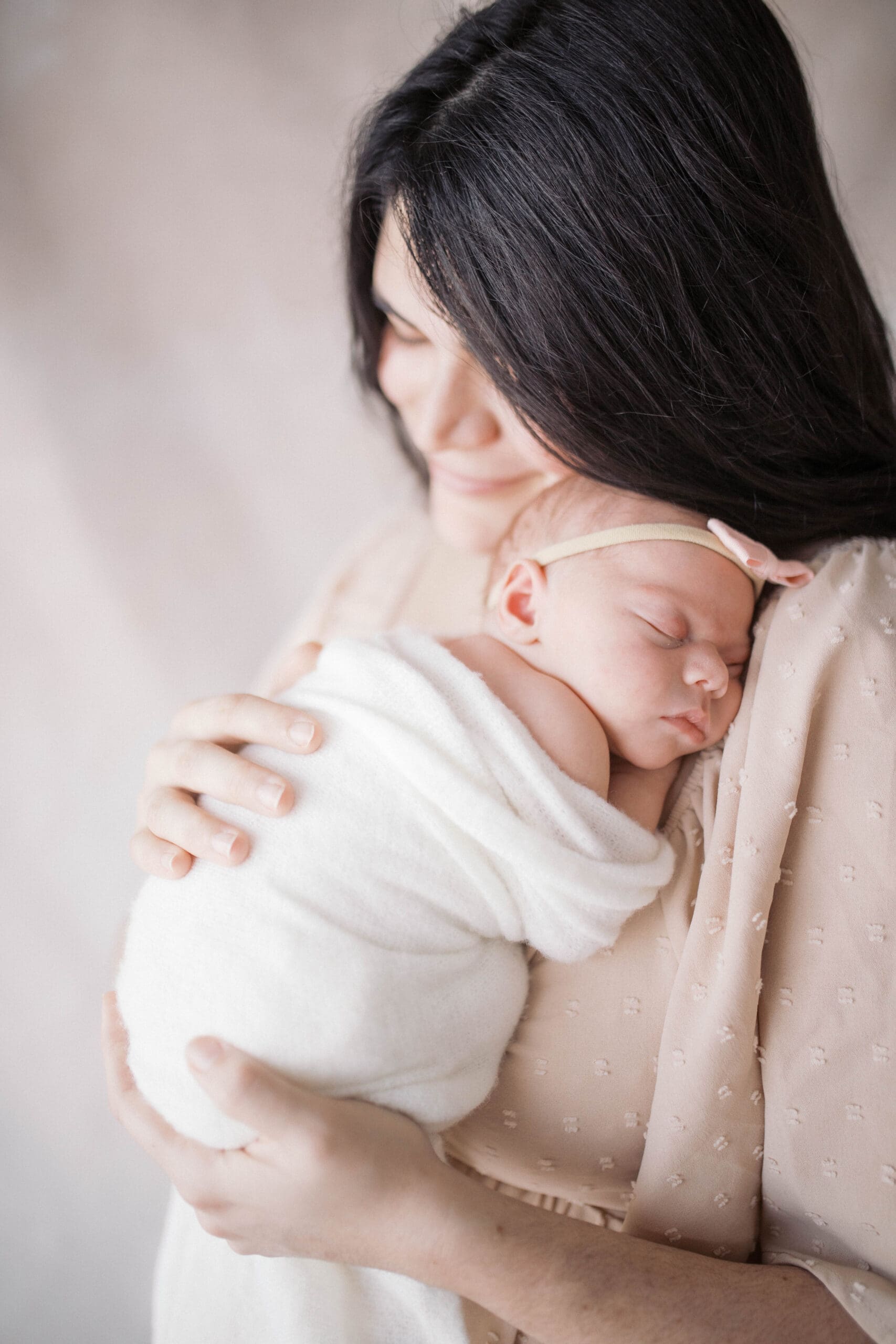 Newborn portrait taken in a studio in Jacksonville of mother snuggling newborn baby girl in front of a neutral backdrop