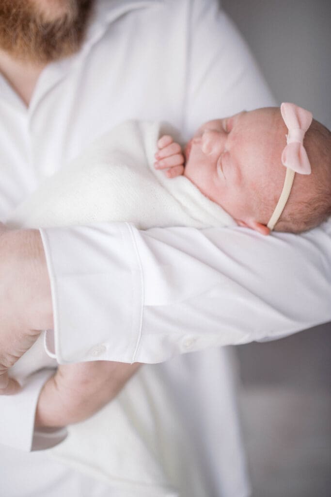 Sleepy newborn boy posed on soft cream blanket in dad's arms by Jacksonville newborn photographer