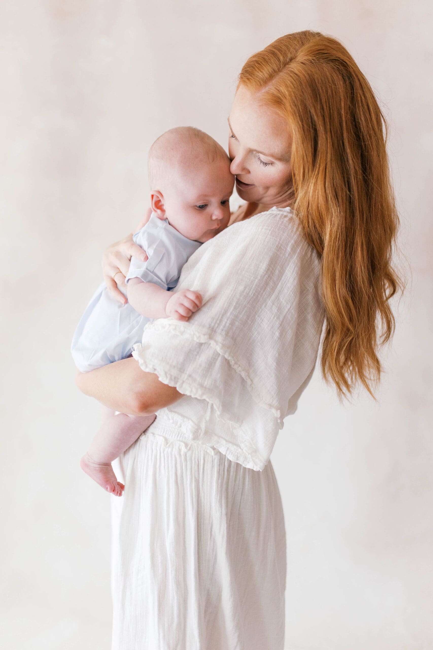 Timeless mother and baby portrait in white clothing against a hand-painted canvas backdrop in Jacksonville, Florida.