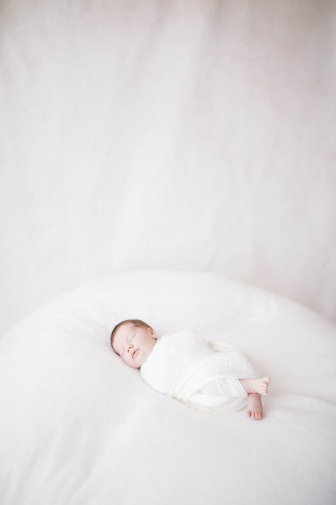 Sleeping baby swaddled in white wrap during newborn photography session in a Jacksonville studio