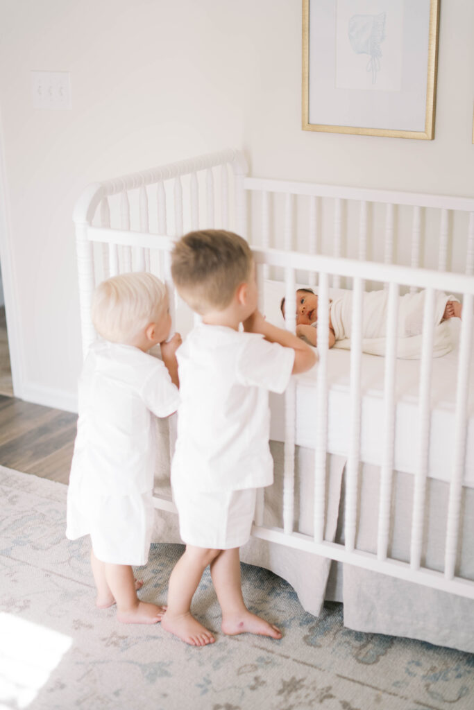 portrait of two older brothers looking at their baby sister in her crib during a Jacksonville in home newborn session
