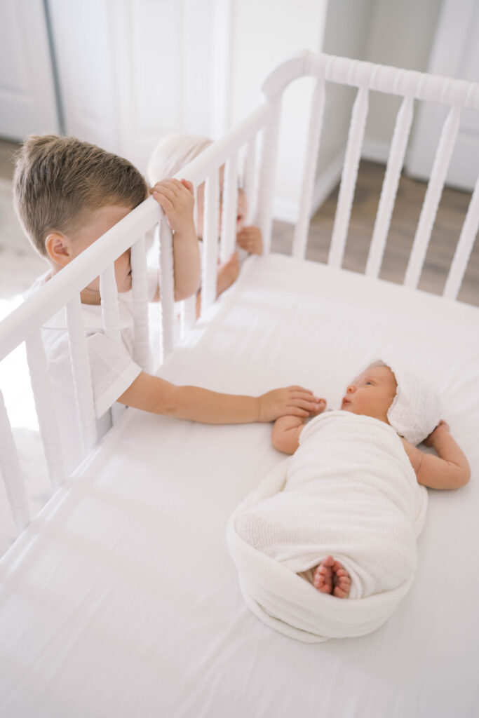Big brother holding newborn baby sister's hand in her crib