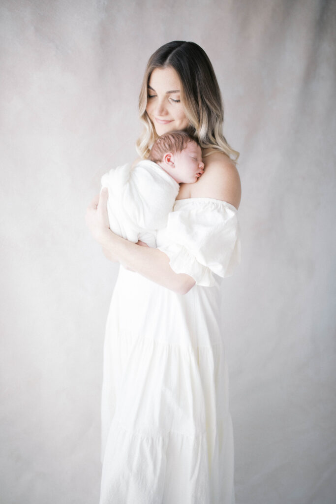 Mother holding newborn baby boy to her chest looking down at him as he sleeps in a Jacksonville portrait studio 
