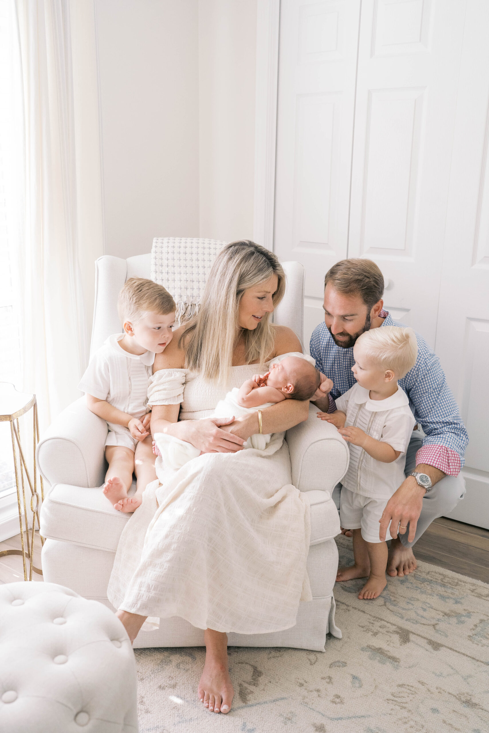 In home newborn portrait in Jacksonville of family of 5 welcoming their baby sister as they gather around her and look at her
