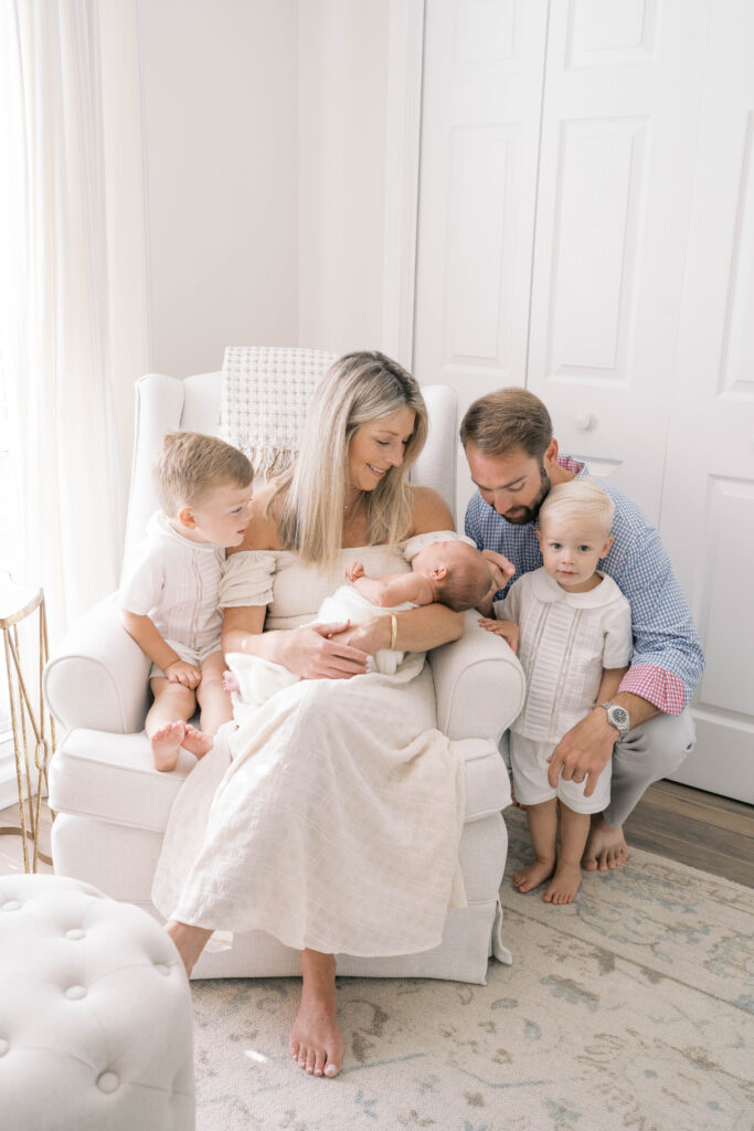 Family portrait of mom dad big brothers all surrounding baby sister to smile at her during a newborn session in Jacksonville
