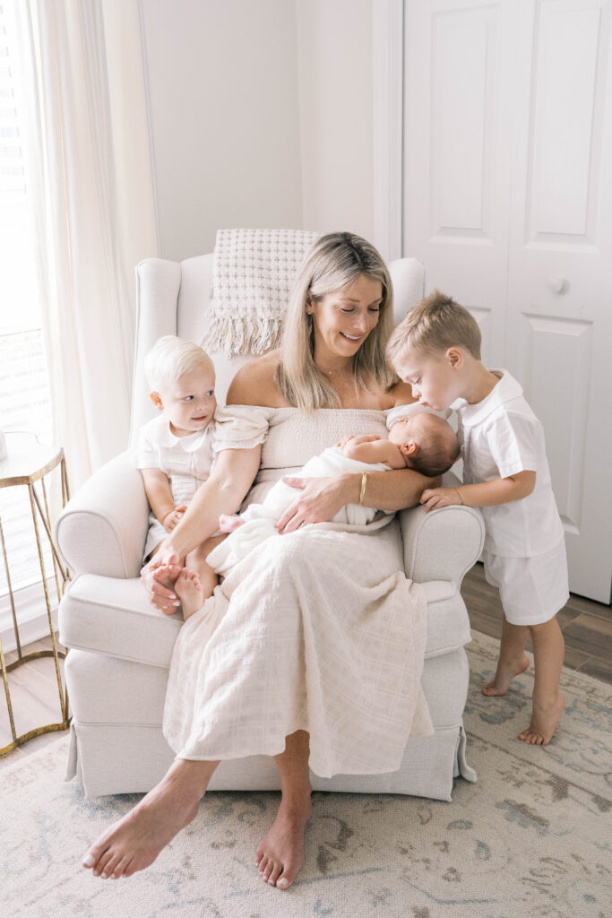 Jacksonville newborn photography session shot in home of mom and two big brothers looking at baby sister as mom rocks her and smiles down at them