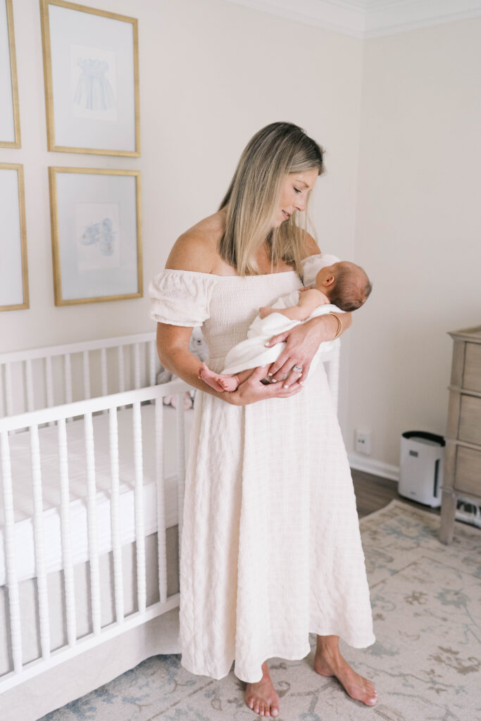 Mother wearing log white off the shoulder dress as she holds her baby girl in her arms while she sleeps