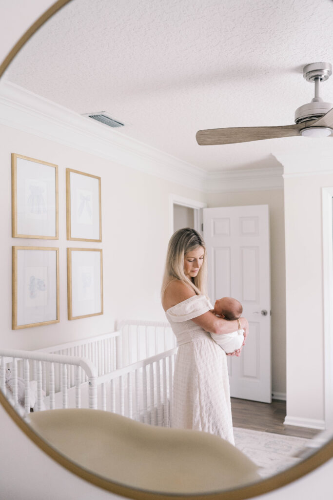 Portrait of mom through the nursery mirror as she sways with her baby girl in her nursery