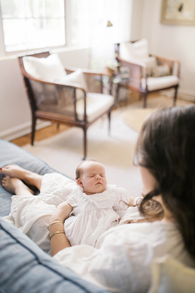 Mom holding newborn baby girl as they relax on the couch in a home in Ortega