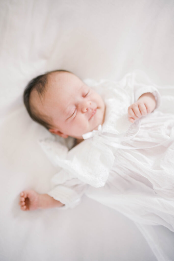 Newborn portrait of a baby girl in a white newborn gown on a white spread