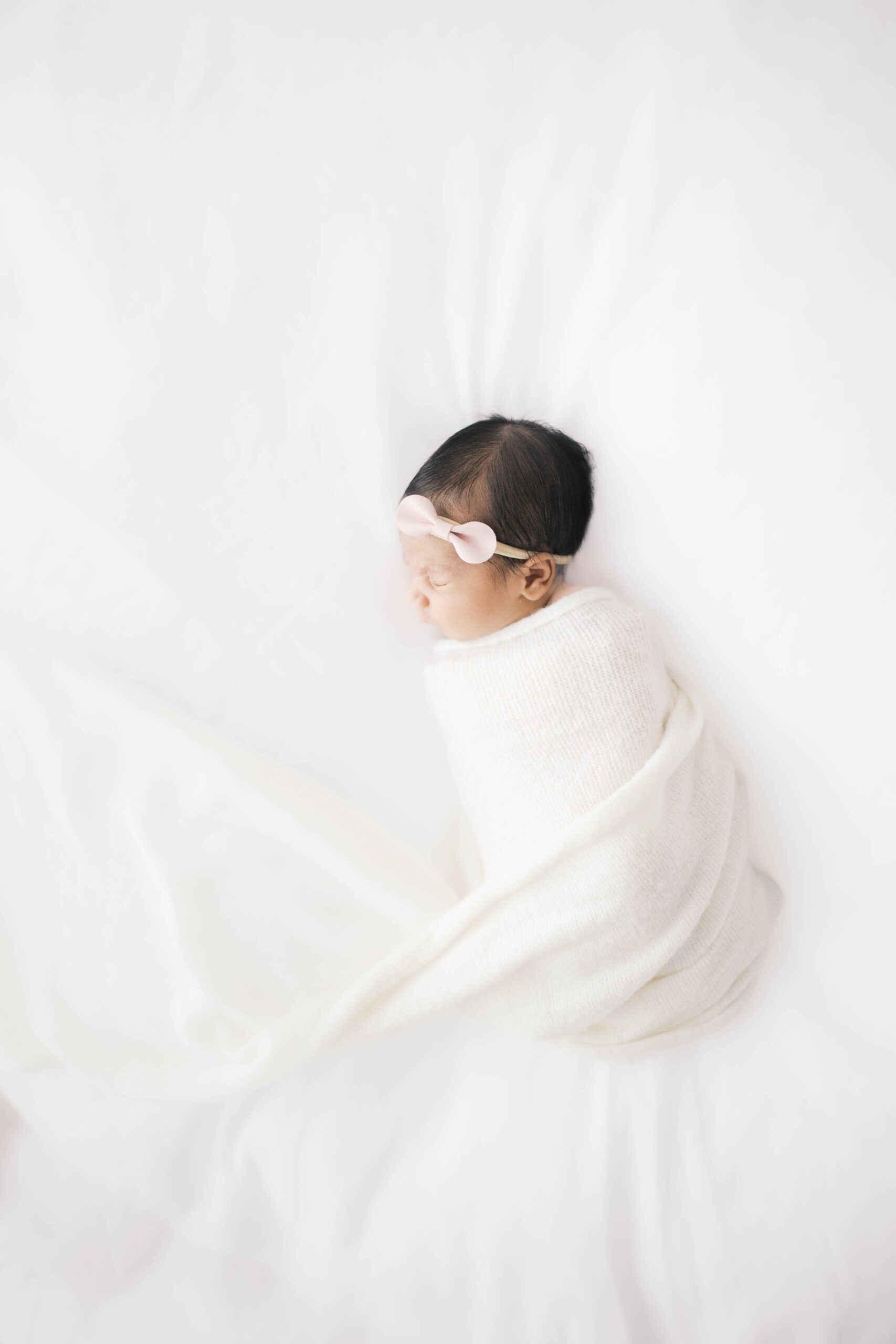 Newborn baby girl swaddled and asleep laying on a white background during a newborn portrait session in a studio in Jacksonville